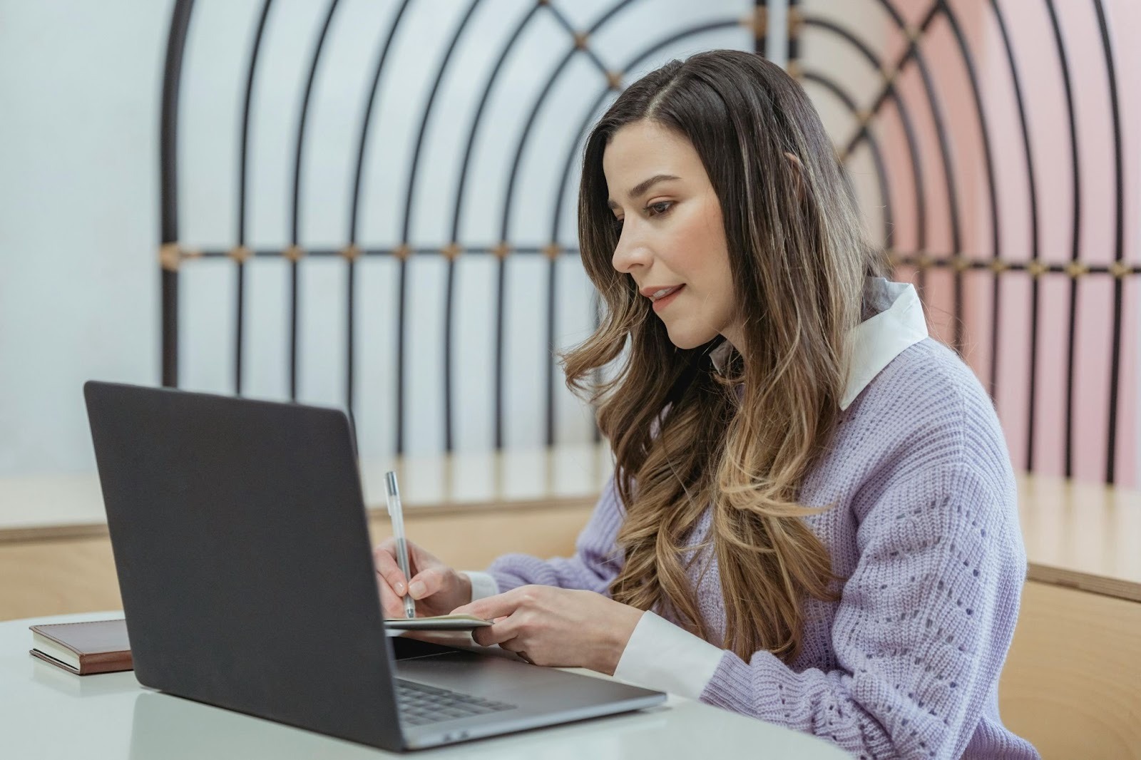 Woman writing in notebook and watching laptop
