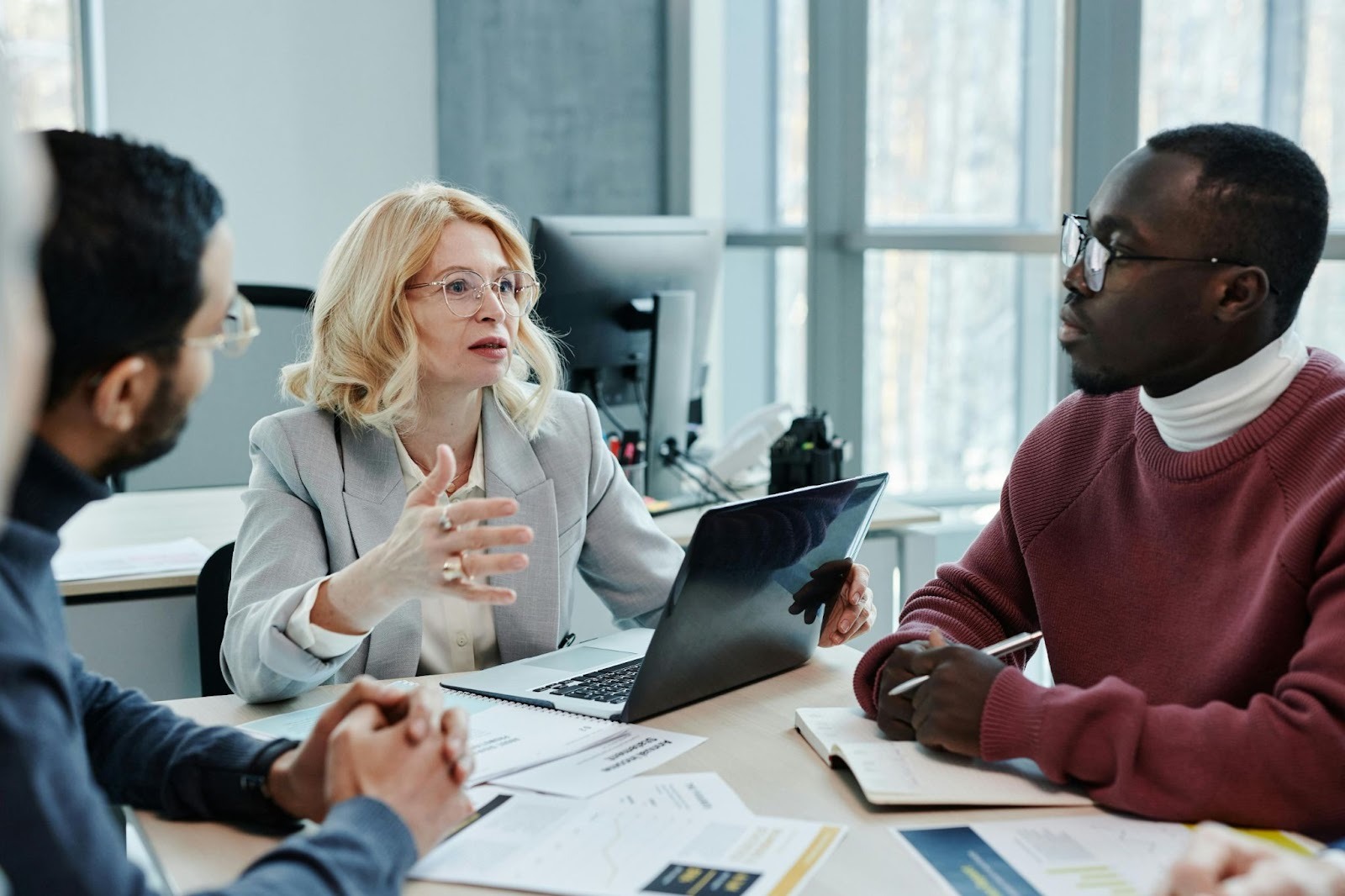 A group of office workers having a meeting at a conference table that has a laptop and papers on it